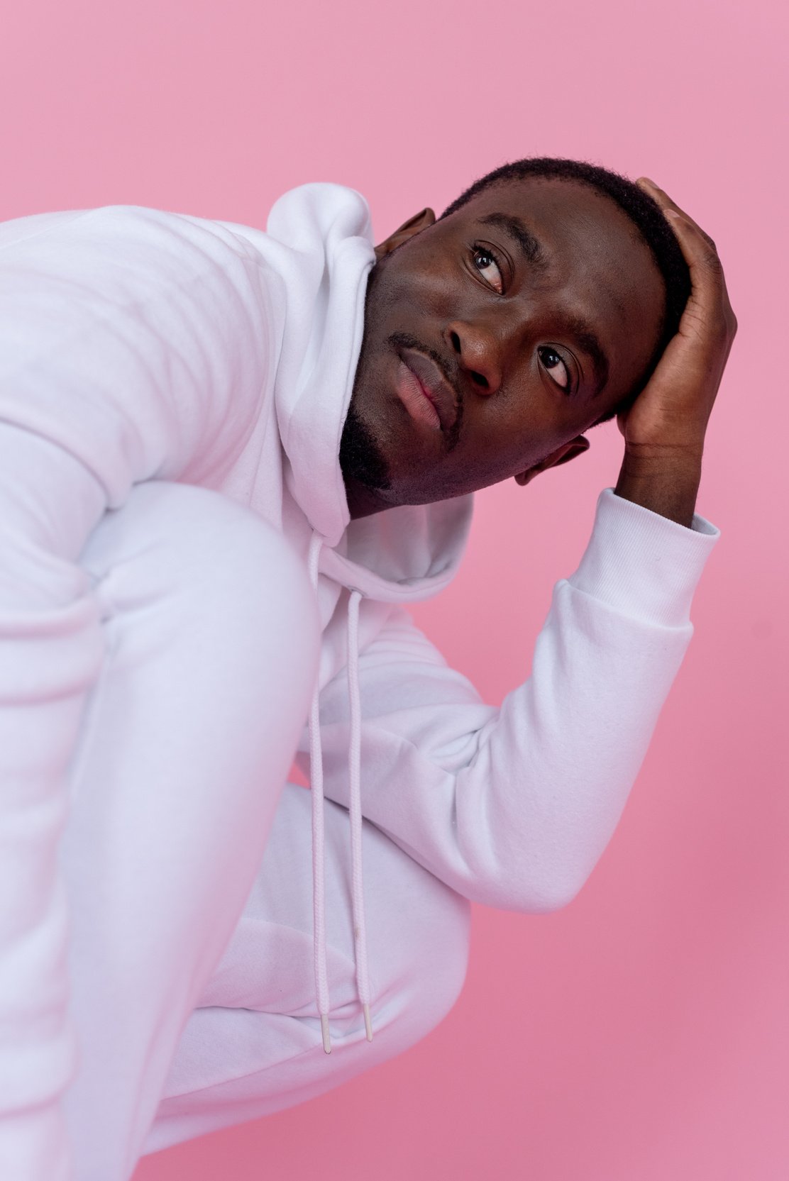 Serious African American male in white outfit on pink background